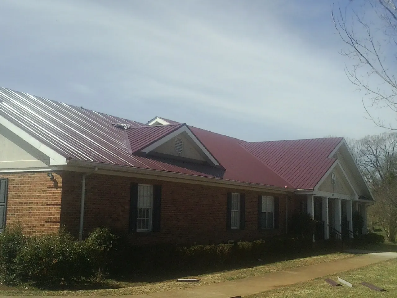Red metal roof with gabled entries on a long brick building, from a Hail Damage Roof Repair job in Halethorpe