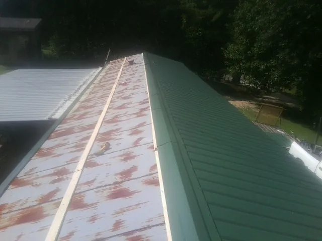 Old rusted panels beside newly installed green metal roofing — Wind Damage Roof Repair by Roofing Brothers in Halethorpe