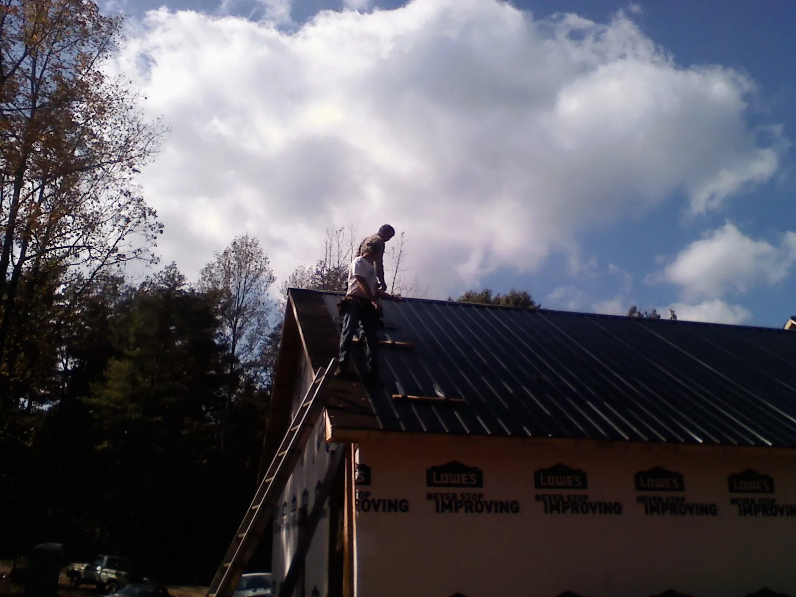 Roofer fastening dark metal panels high against a cloudy sky, from a Roof Inspection job in Halethorpe